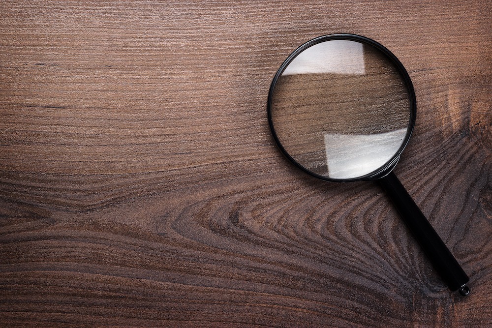 Zwart vergrootglas liggend op een houten oppervlak, beeld bij een fiscale audit of controle